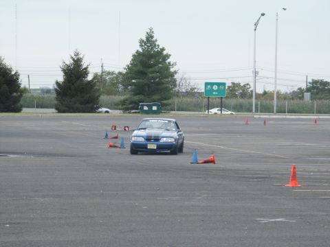 2001 Mercury Grand Marquis - A blue Ford Mustang navigates a cone course in a large paved area, with another vehicle in the distance.