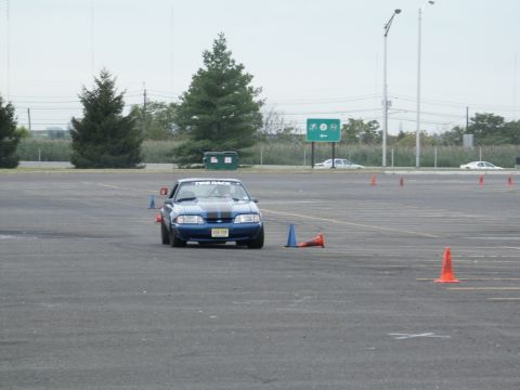 2001 Mercury Grand Marquis - A blue Ford Mustang navigates a course marked by orange cones, with other vehicles in the background.