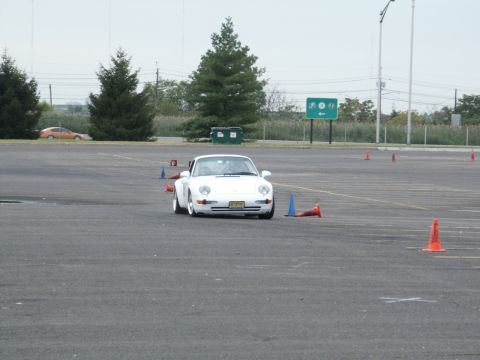 2001 Mercury Grand Marquis - A white Porsche 911 is seen on a paved lot, maneuvering through an autocross course marked by traffic cones.