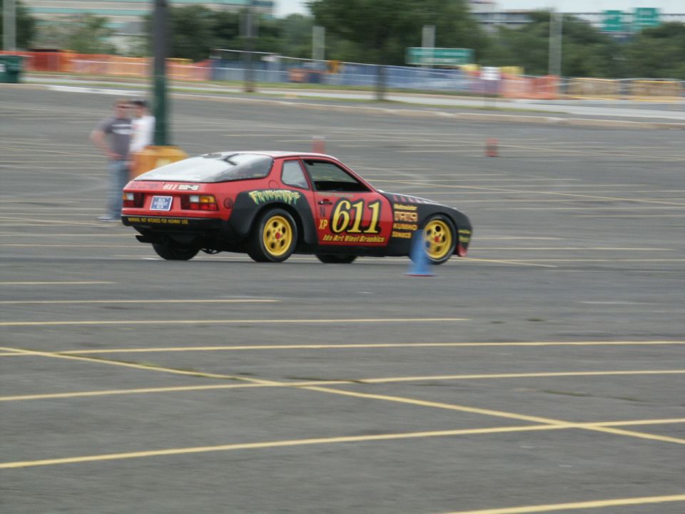 Porsche 944 race car with number 611 on door, yellow wheels, and racing decals, on asphalt track