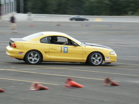 2001 Mercury Grand Marquis - A yellow coupe with racing stripes navigates a track, with another car blurred in the background.