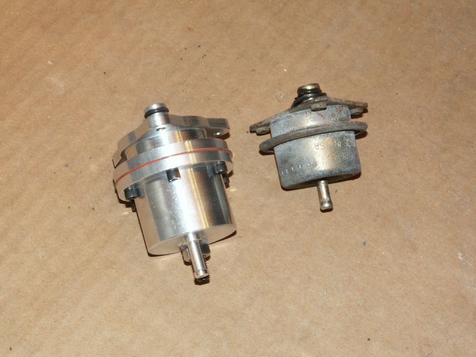 Two fuel pressure regulators, one shiny aluminum and one older metal one, sit on a brown surface