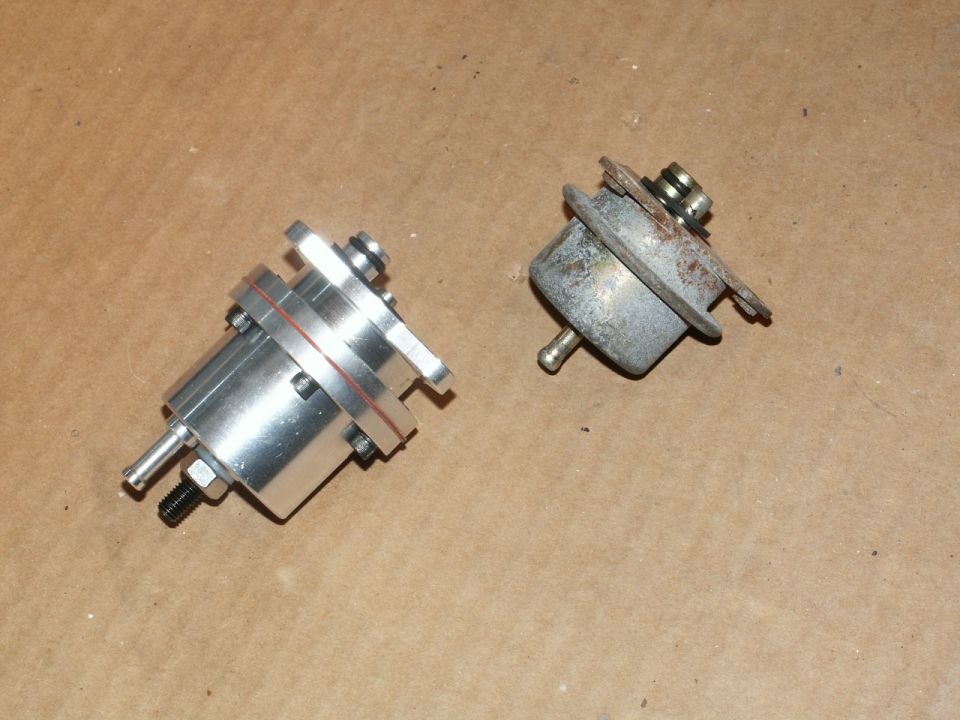 Two fuel pressure regulators, one new aluminum and one old rusty metal, on a brown surface