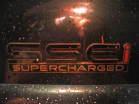 1992 Ford Crown Victoria - A close-up view of a "SSEi SUPERCHARGED" emblem is visible on a dark, wet surface.