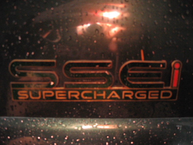 Close-up of a "SSEi SUPERCHARGED" badge on a dark, wet surface