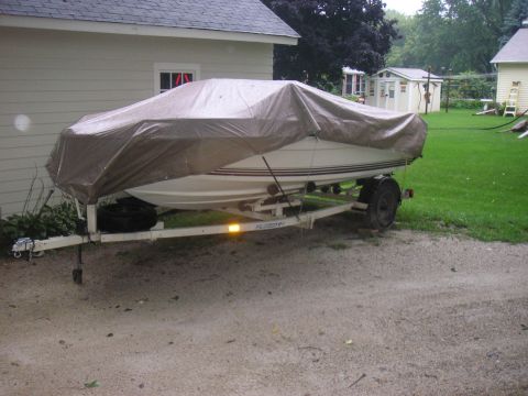 1979 Four Winns 170 Horizon - A covered boat sits on a trailer in a driveway next to a residential building.