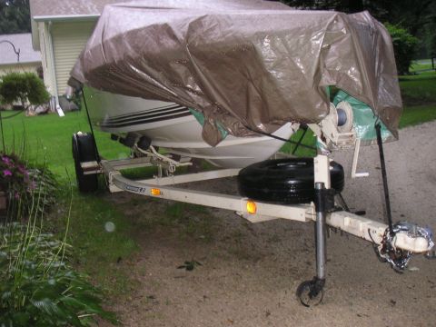 1979 Four Winns 170 Horizon - A boat on a trailer is covered with a tarp, parked outdoors near a house.