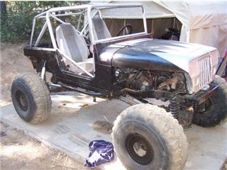 1986 Ford Bronco - Modified Jeep CJ-7 body with roll cage and exposed engine bay, in what appears to be a workshop.