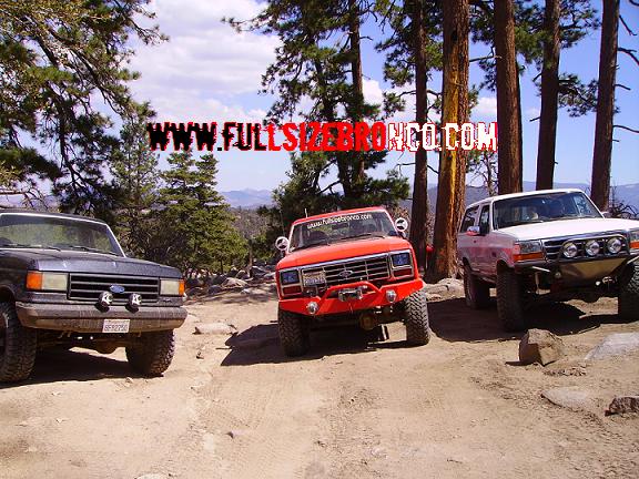 1990 Ford Bronco and two other SUVs parked on a dirt road with trees and mountains in background
