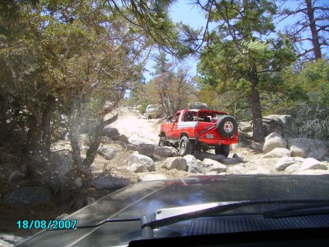 1990 Ford Bronco - This red SUV is navigating a challenging, rocky off-road path with another vehicle visible ahead.