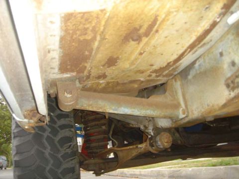 1984 Ford Bronco - The underside of the vehicle shows significant rust and wear on the frame and suspension parts.