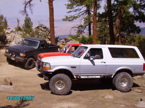 1990 Ford Bronco - A silver SUV with off-road tires is parked on a dirt road with two other vehicles behind it.