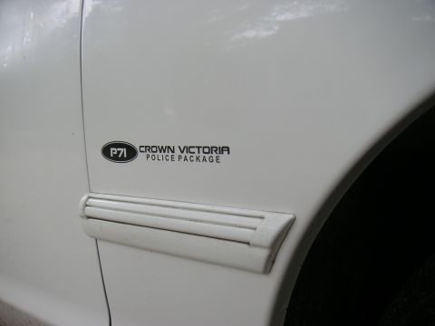 1997 Ford Crown Victoria - Close-up of a white car's fender showing a "Crown Victoria Police Package" badge and trim.