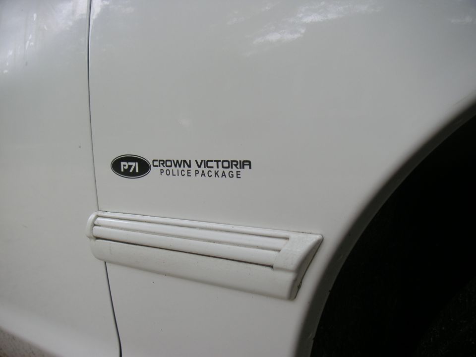 White car fender with a black oval badge reading "P71 CROWN VICTORIA POLICE PACKAGE" and a white trim piece