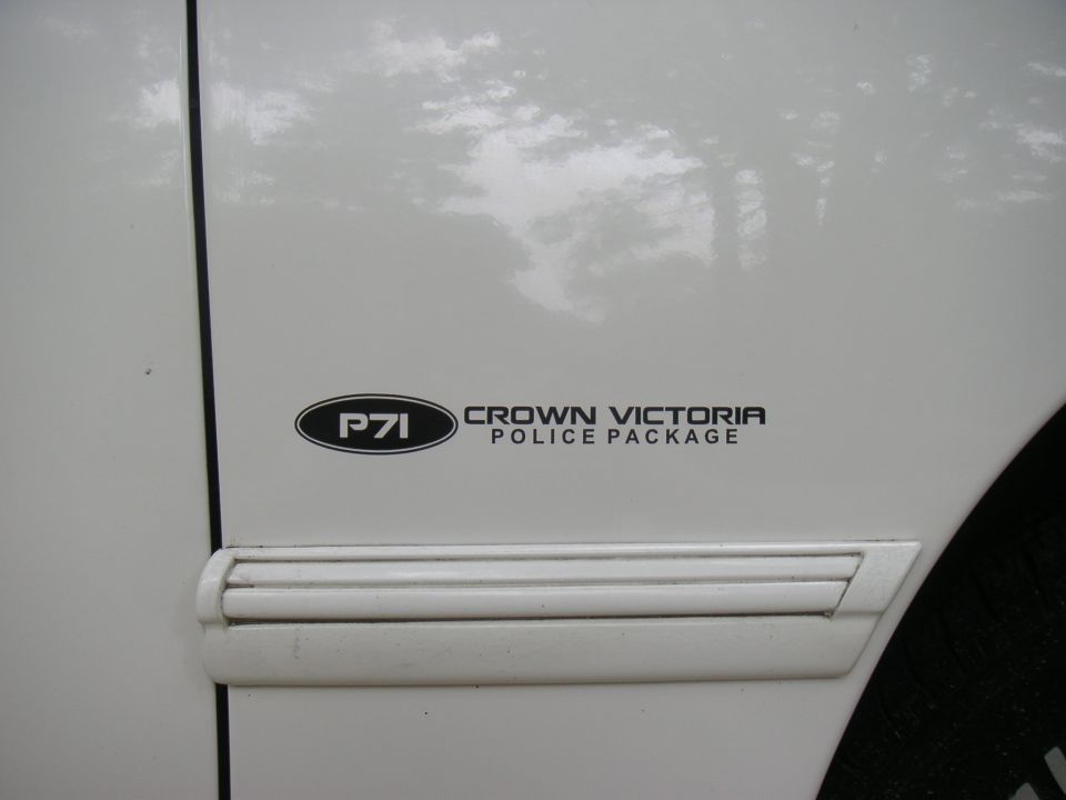 White car door with a black oval sticker reading P71, and text Crown Victoria Police Package. A horizontal trim piece is below the sticker