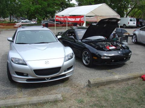 1986 Mazda RX-7 - A black Mazda RX-7 is parked with its hood open, revealing the engine bay. Another Mazda is parked to its left.