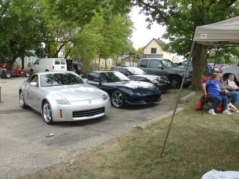 1986 Mazda RX-7 - Several cars are parked in a lot, with people relaxing under a canopy on-site tent.