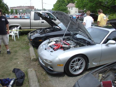 1986 Mazda RX-7 - Two Mazda RX-7s are parked side-by-side with their hoods open, displaying their engines.