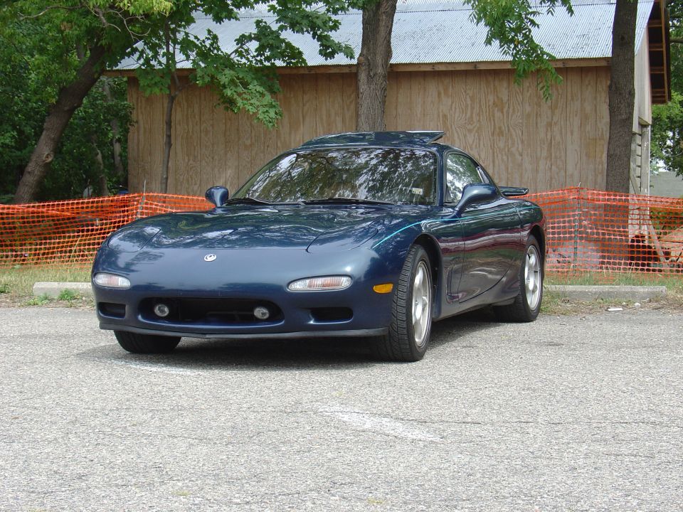 Dark blue Mazda RX-7 with a sunroof, parked outdoors. The car has a visible front bumper with fog lights and a spoiler