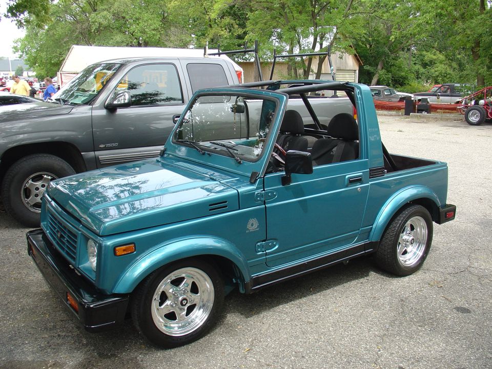 Teal convertible SUV with black trim and chrome wheels parked next to a gray pickup truck