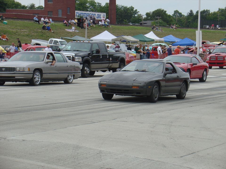 Dark gray 1986 Mazda RX-7 driving on a track, front-right quarter view