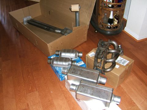 1991 Ford Bronco - Various exhaust system components, including a manifold, catalytic converters, and mufflers, are laid out on a hardwood floor.
