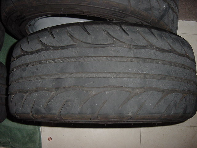 Close-up of used low-profile tire tread on a tiled floor with wheels stacked behind