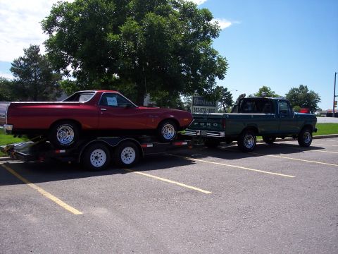1972 Ford Ranchero - A red 1972 Ford Ranchero is transported on a trailer pulled by a green Ford pickup truck in a parking lot.