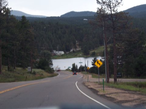 1972 Ford Ranchero - A scenic drive passes by a lake surrounded by dense forest and rolling hills under an overcast sky.