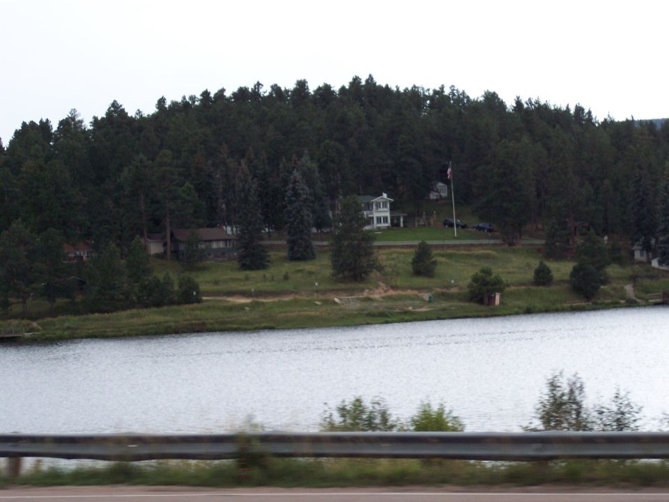 Lake and forested hillside with houses across the water, guardrail in foreground.