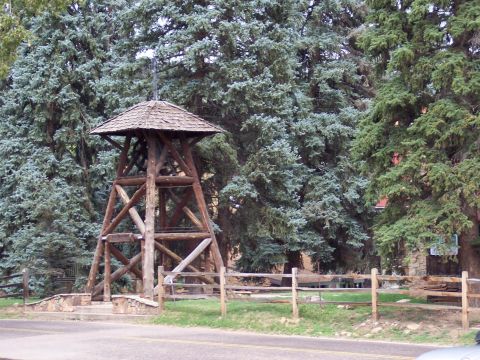 1972 Ford Ranchero - A rustic wooden bell tower stands amidst tall evergreen trees, with a split-rail fence in the foreground.