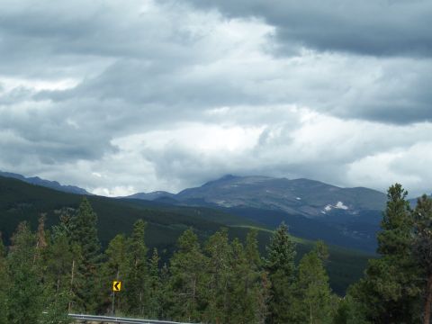 1972 Ford Ranchero - A scenic mountain vista with dense pine forests and dramatic clouds overhead, a road sign is visible.