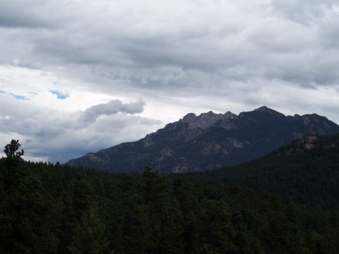 1972 Ford Ranchero - A mountain range is shrouded in dark, dramatic clouds, with a dense forest in the foreground.