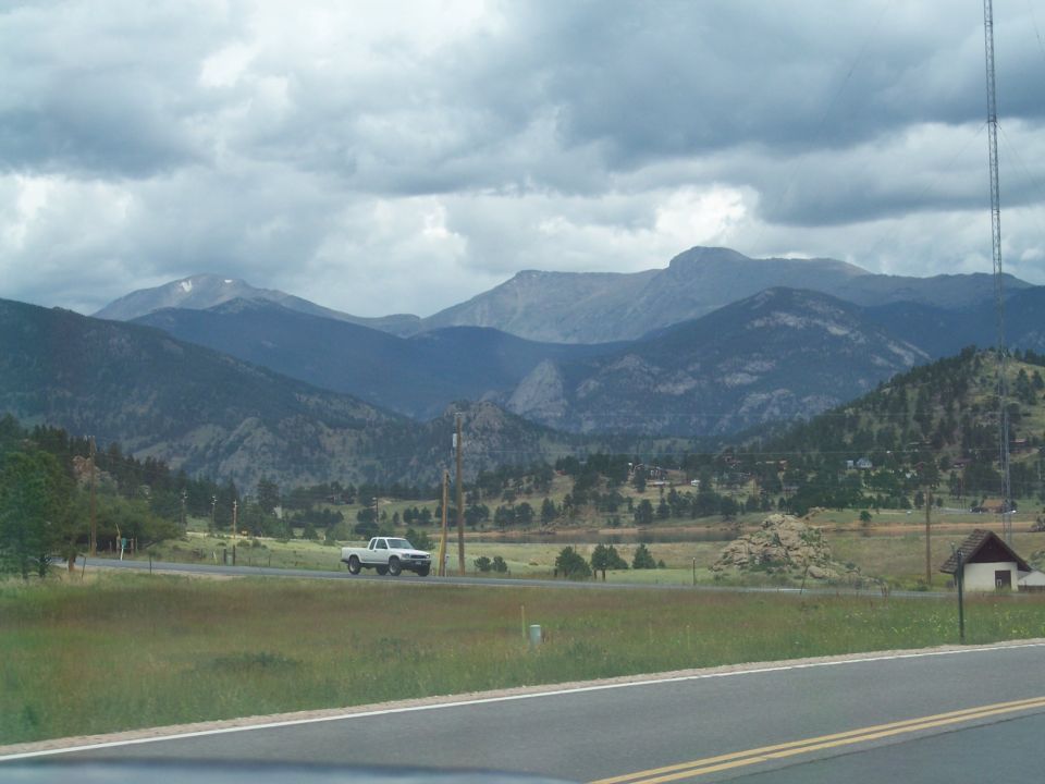 White pickup truck on a rural road with forested mountains under cloudy skies