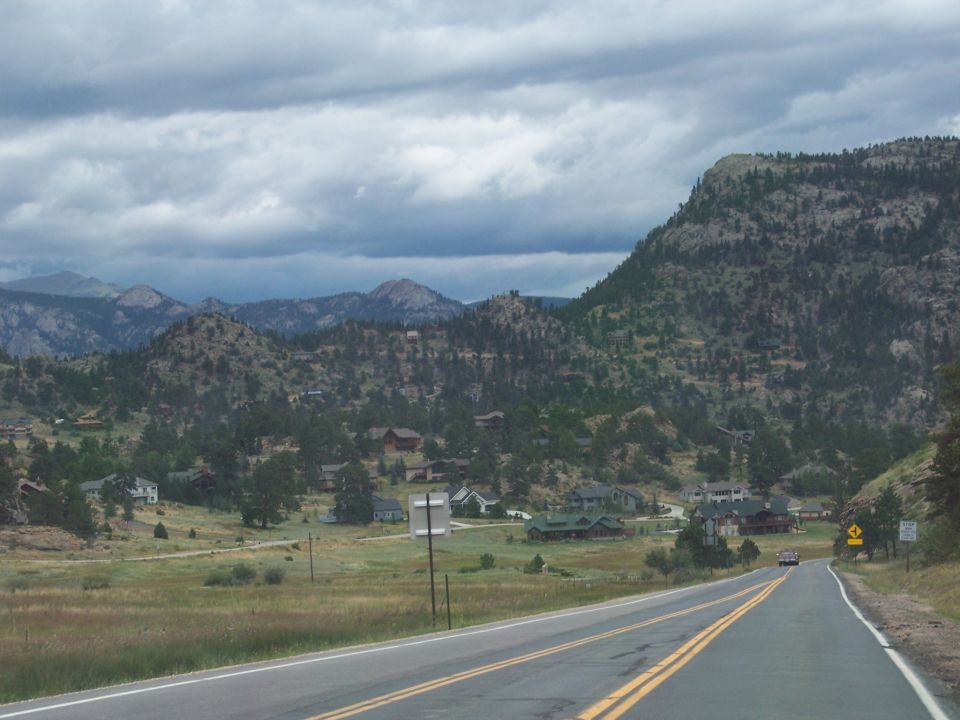 Mountain highway winding through a valley with scattered homes under cloudy skies