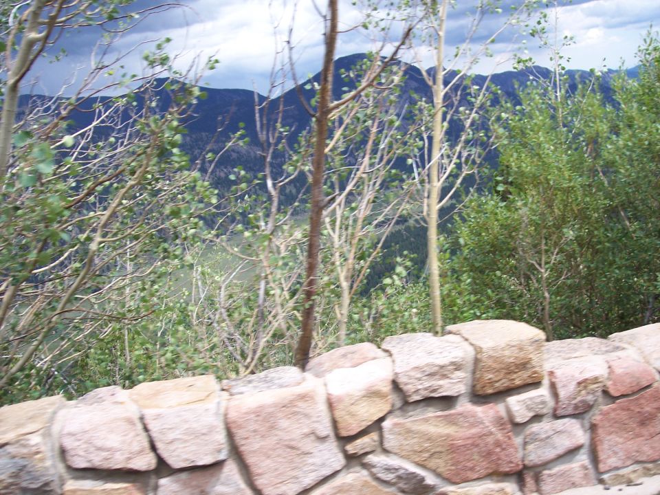 Stone wall with trees and mountains under cloudy sky, no vehicle present