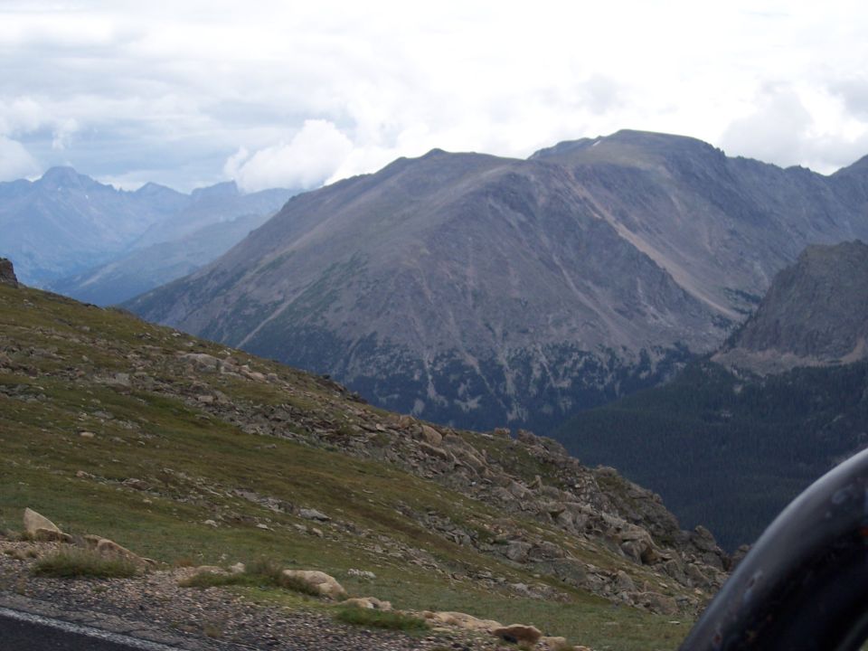 Rocky mountain range under cloudy sky with vehicle edge at lower right