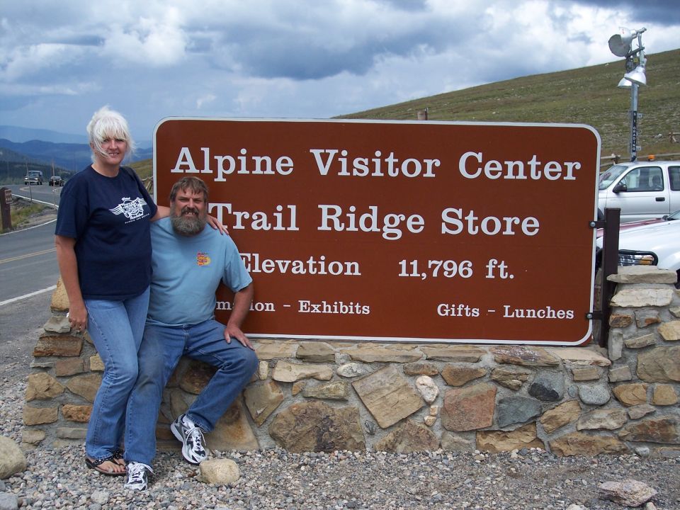 Couple posing beside Alpine Visitor Center elevation sign in mountains