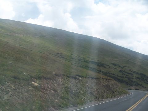 1972 Ford Ranchero - A winding road cuts through a mountain landscape with sparse vegetation and scattered clouds overhead.