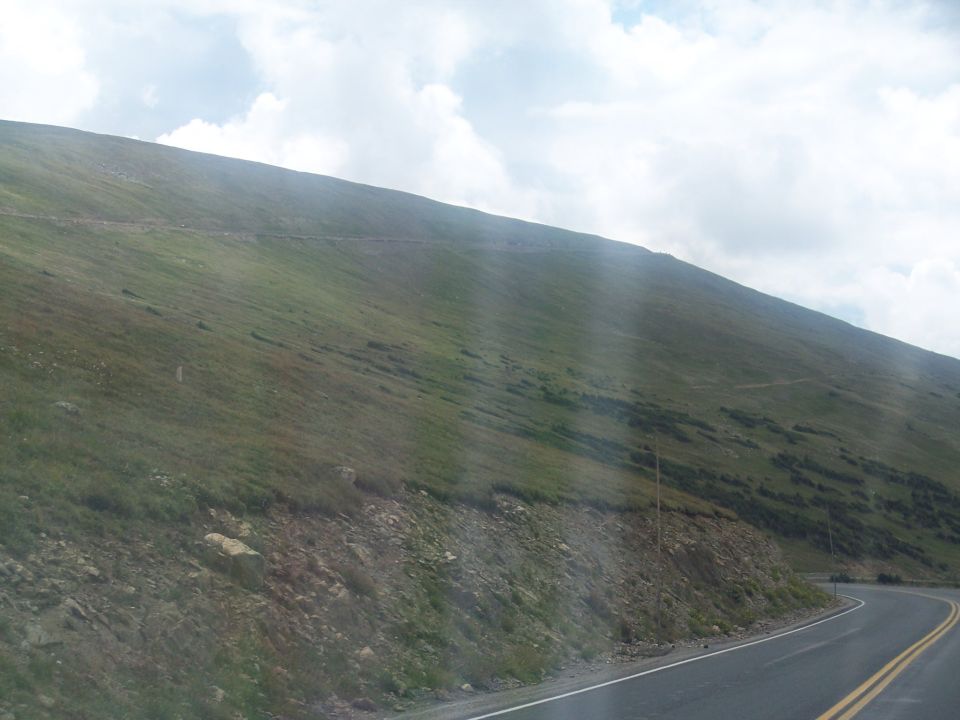 Grassy mountain slope beside a curving two-lane road under cloudy sky