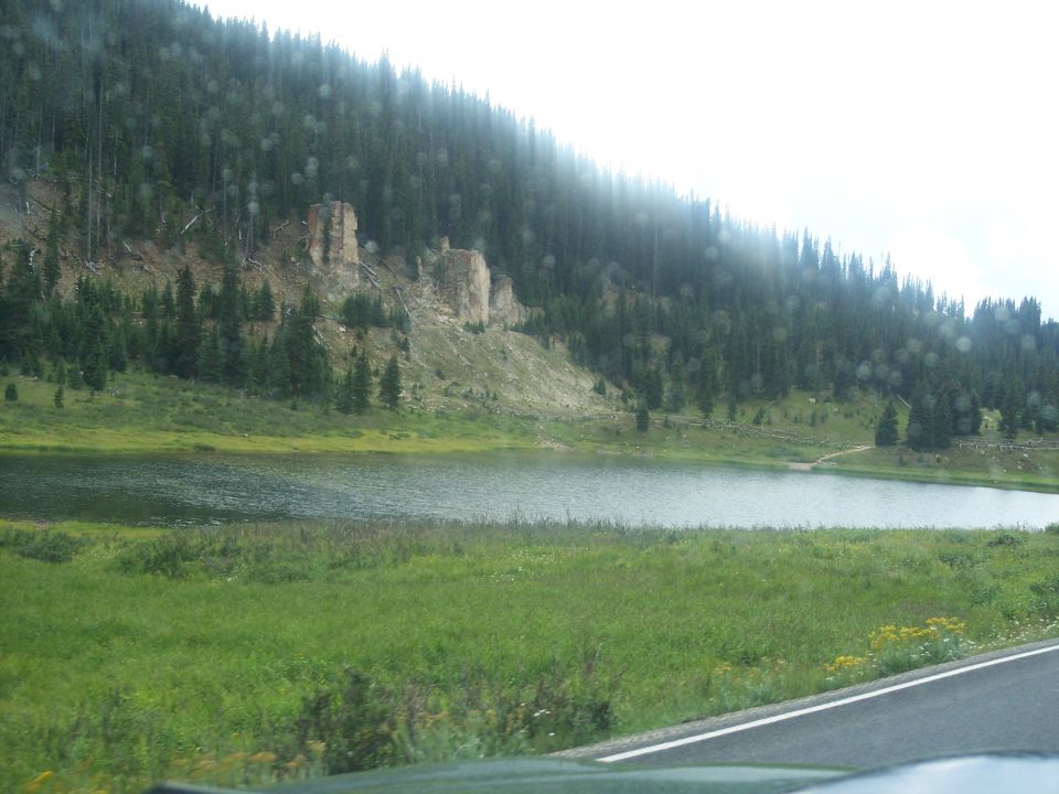 Mountain lake and forested hillside seen through a windshield from inside a car
