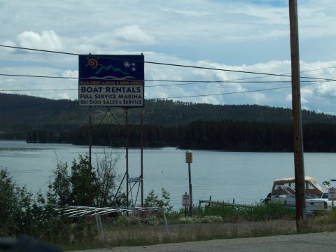 1972 Ford Ranchero - A sign advertises boat rentals and marina services next to a calm lake with a treed shoreline.