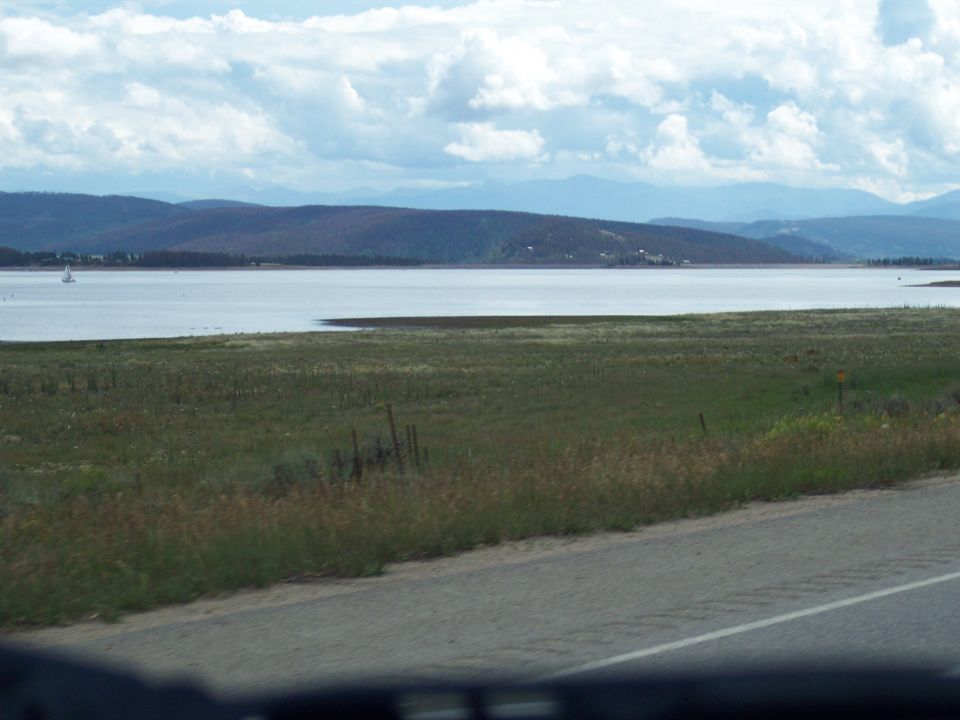 Lake and mountains seen from a car window across a grassy field and road