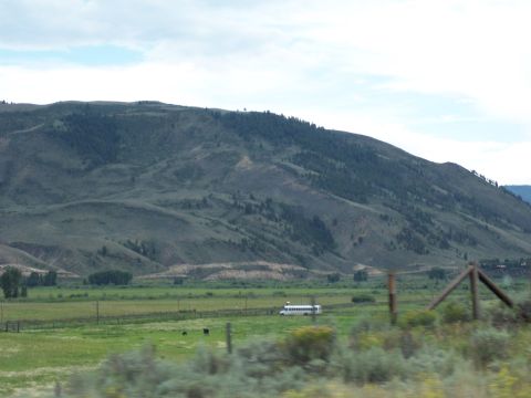 1972 Ford Ranchero - A white bus travels across a wide, green field under a partly cloudy sky, with distant hills forming the horizon.