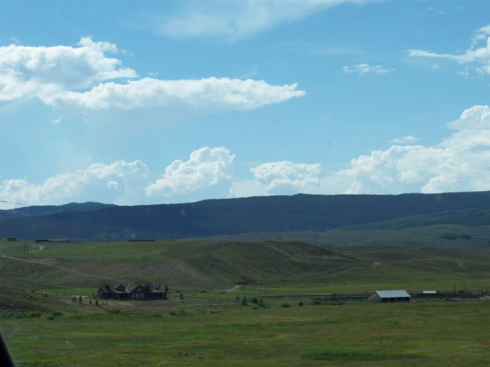 Rural landscape with a house, hills, and cloudy sky; no vehicle visible