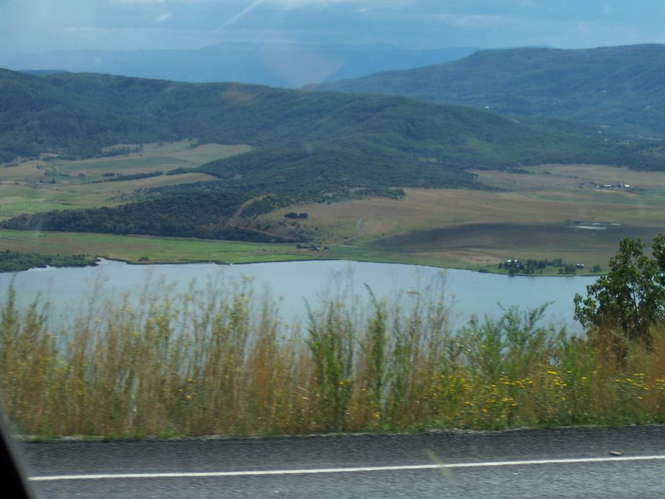 Roadside view of a lake and forested hills with grass in foreground