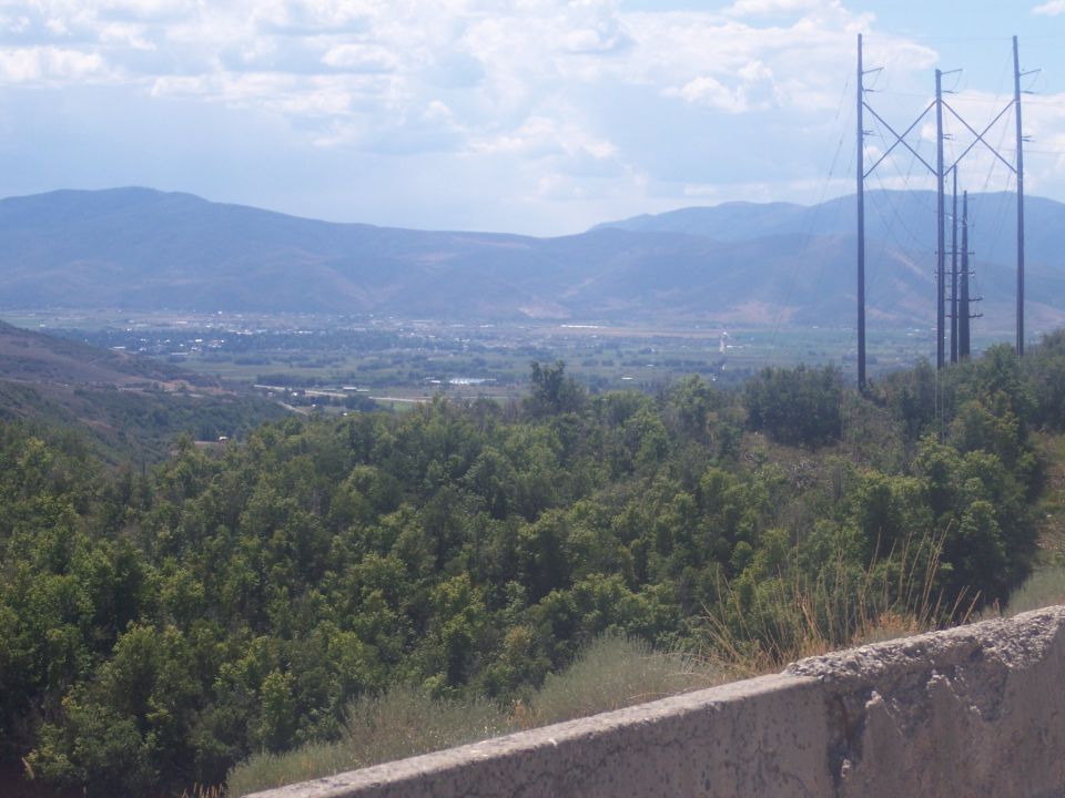 Valley and mountain landscape with power transmission towers under a cloudy sky.