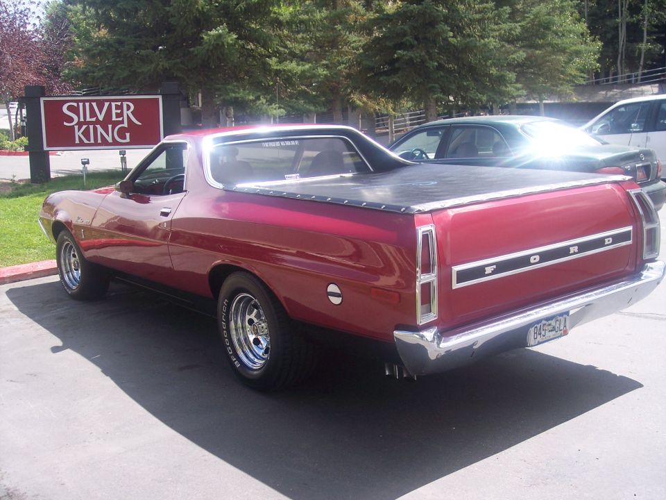 Red Ford Ranchero car-pickup viewed from rear three-quarter, parked near Silver King sign