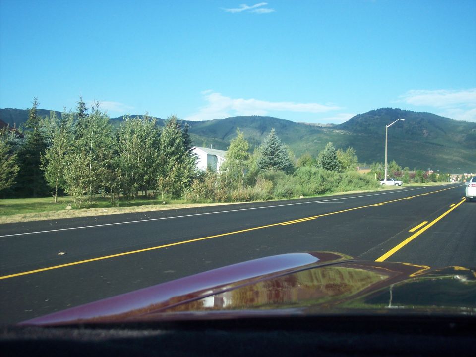 Maroon car hood in foreground with a paved road and mountains ahead