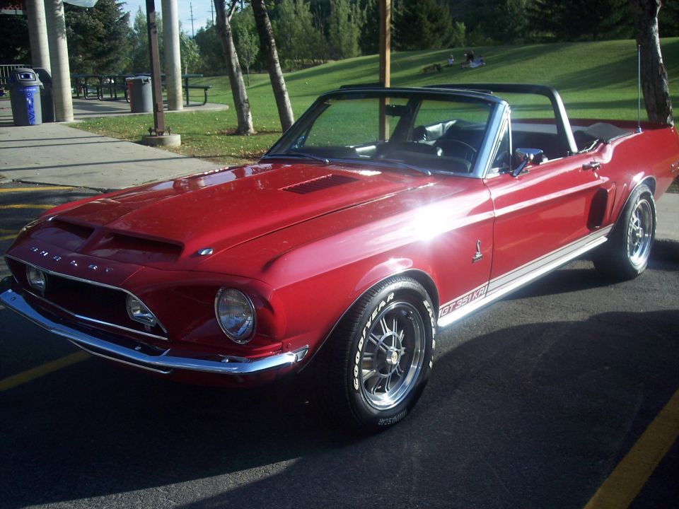 Red Shelby Mustang convertible with white stripes parked in lot, front-left view